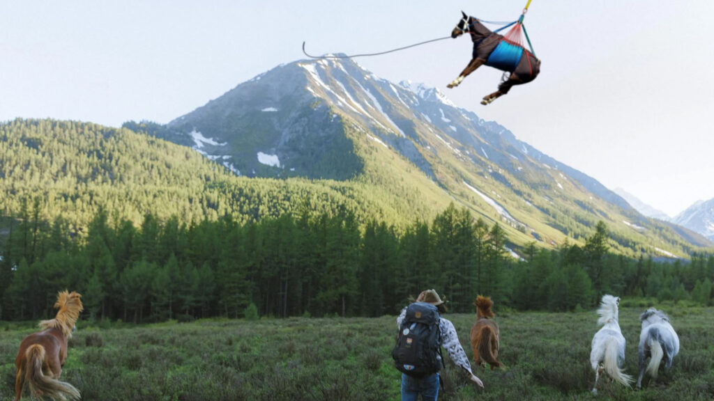 A backpacker chases wild horses through a beautiful field with mountains in the background while another horse is airlifted by a helicopter 