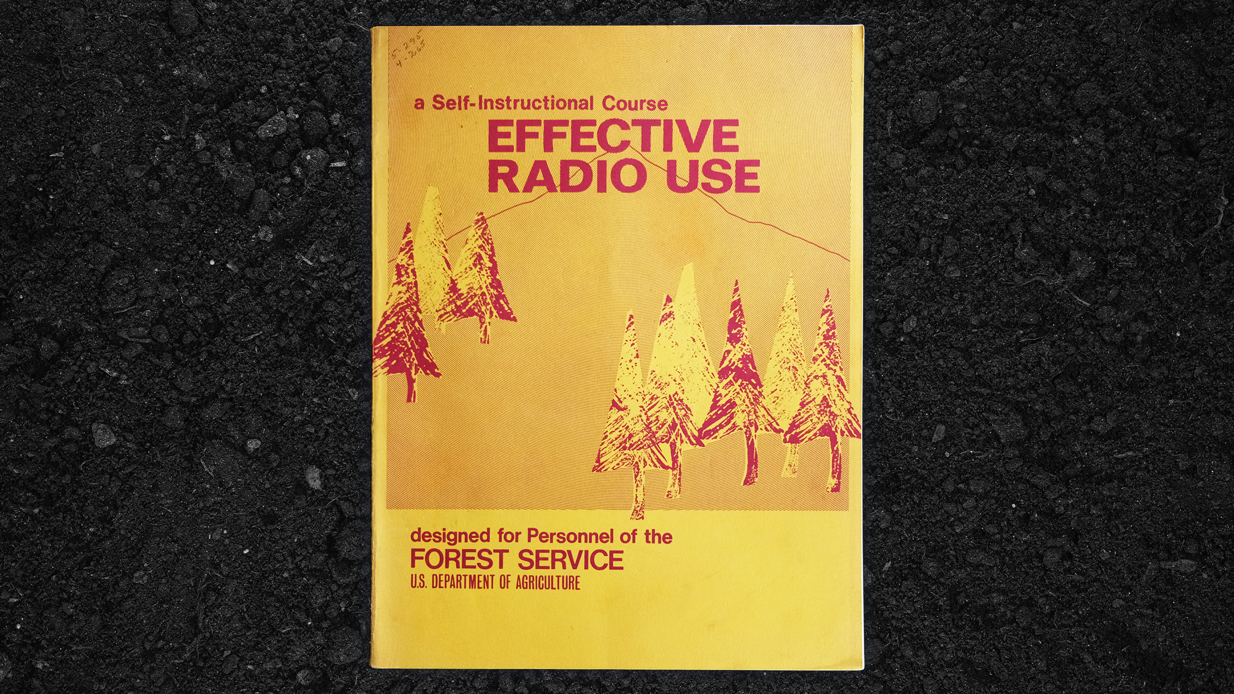 The cover of a Self-Instructional Course: Effective Radio Use (19690 by the US Forest Service sitting on black dirt - the book is bright yellow and orange