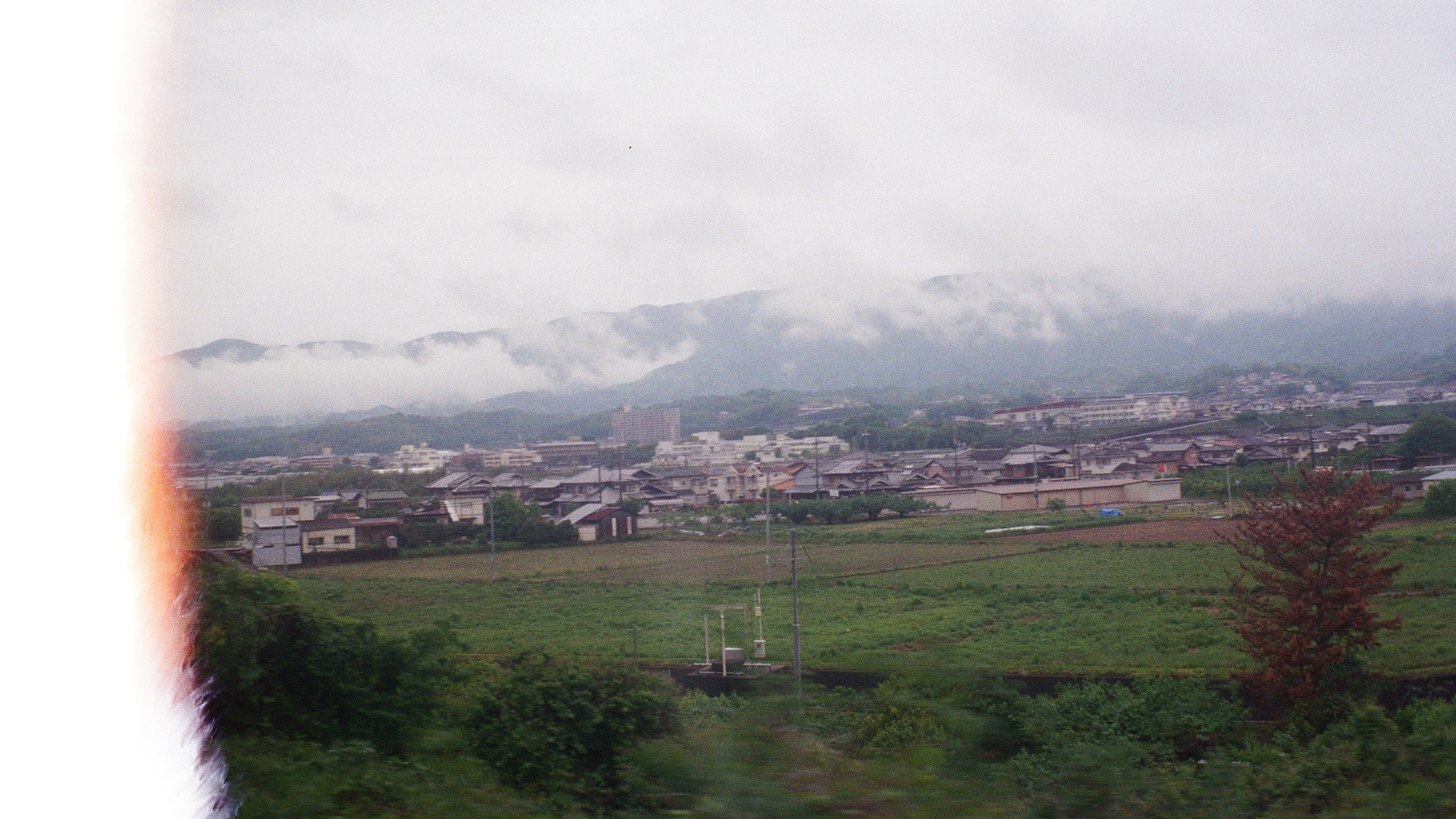 A washed out film photo of a rural Japanese landscape as seen from a passing train