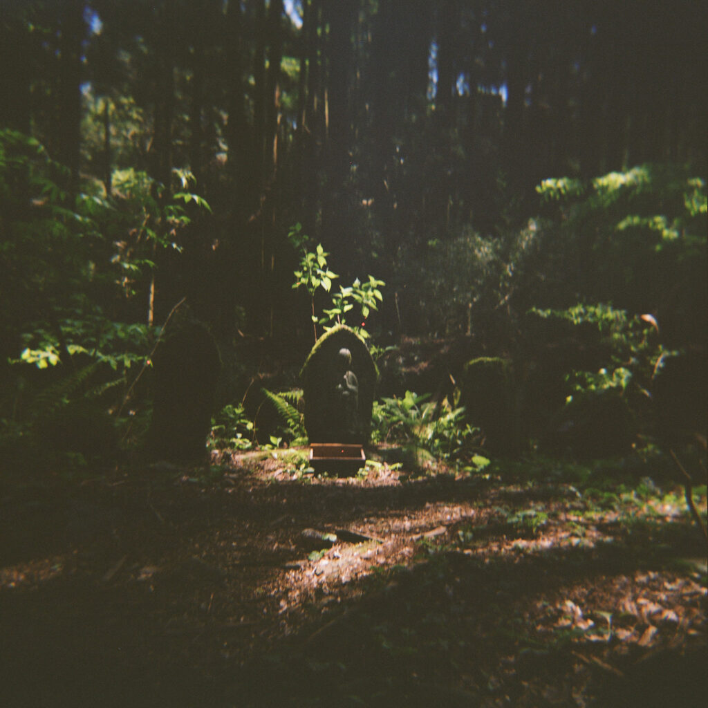 A little shrine statue covered in moss in a Japanese forest